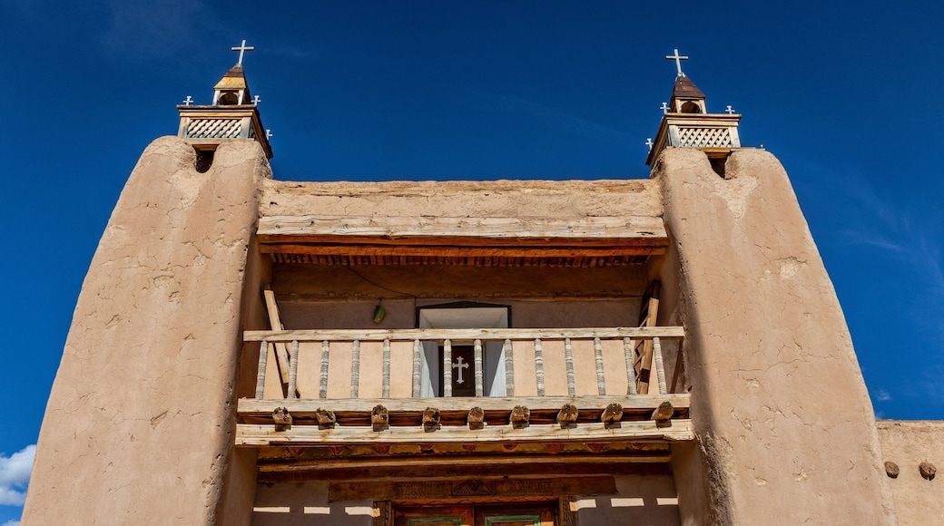 A building with a balcony, a wooden door, and two towers with crosses on top.