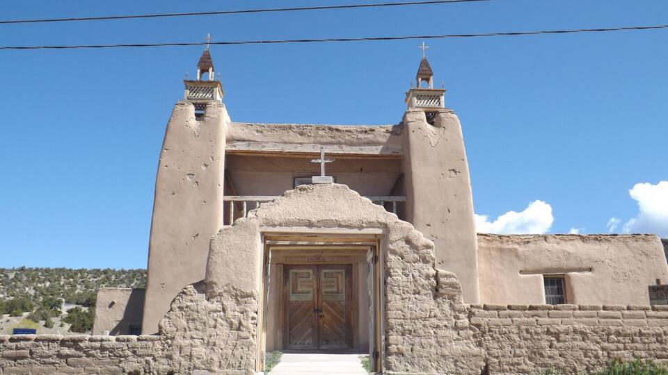 A historic church with a prominent cross on top, a wooden door, and two bell towers.