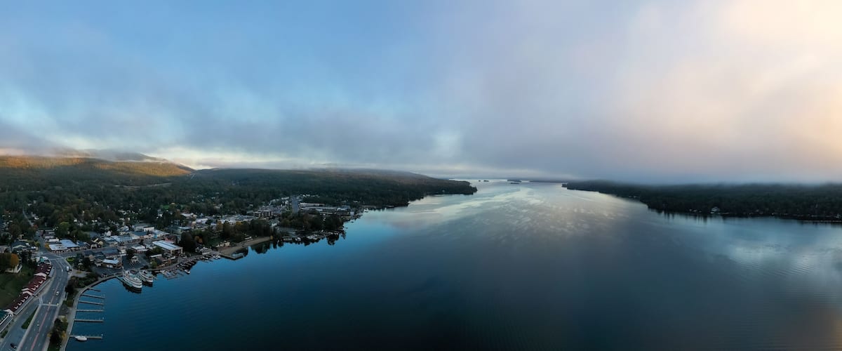 A calm lake surrounded by forested hills and a small town with docks and boats.