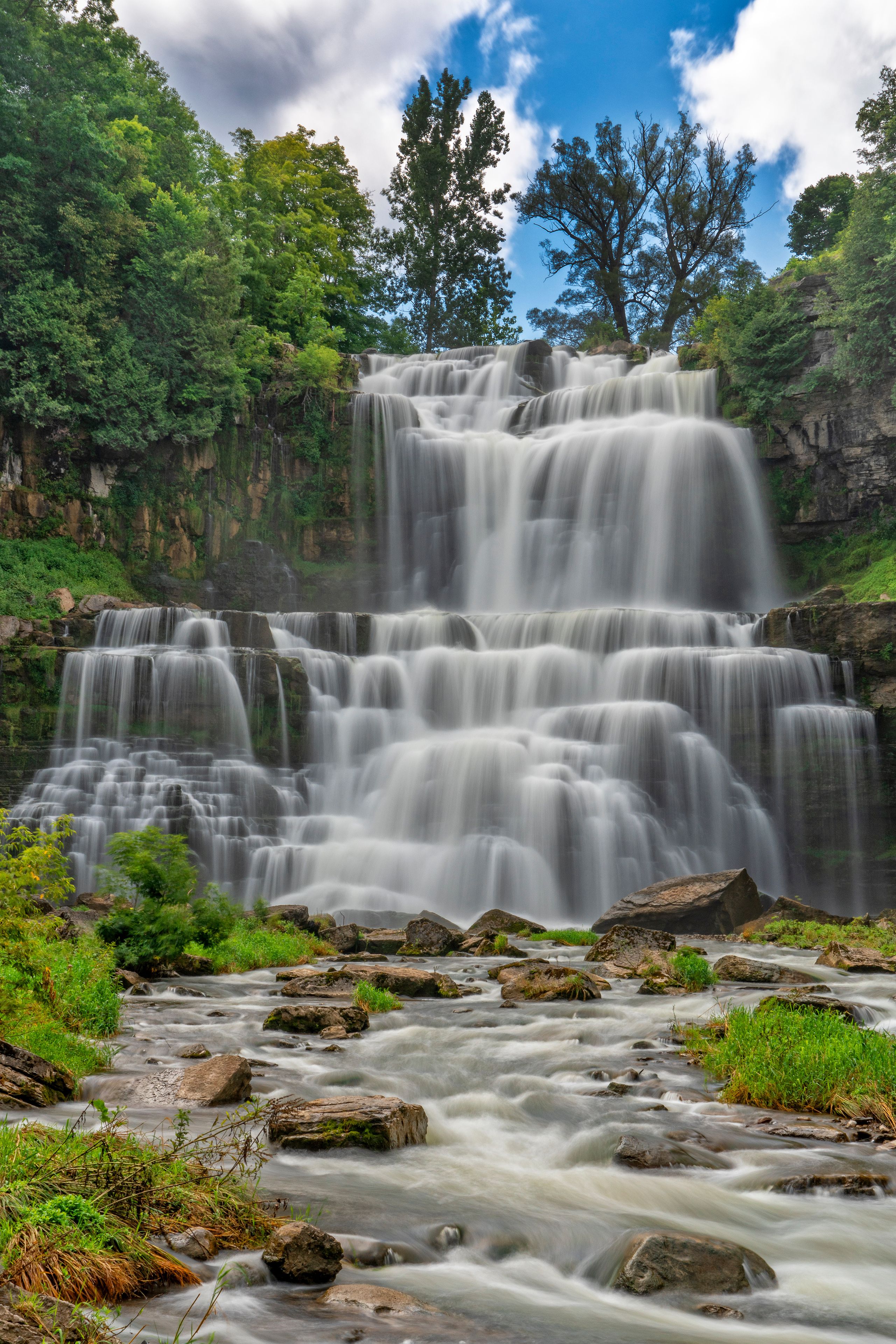 Ein mehrstufiger Wasserfall, umgeben von üppiger Vegetation und felsigem Gelände.