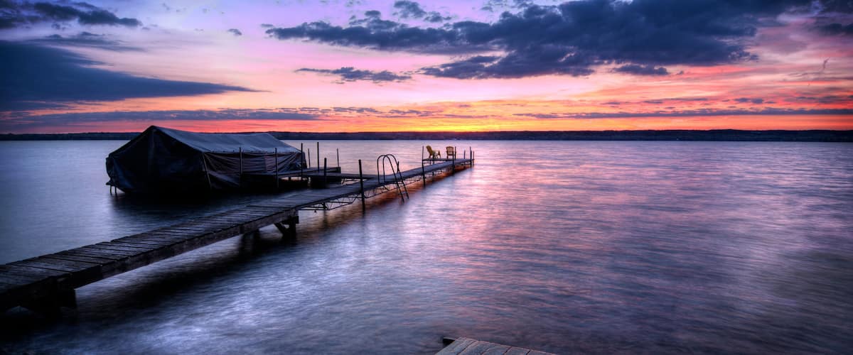 Een houten steiger die zich uitstrekt over kalm water, met een overdekte constructie op de steiger en een zonsonderganglucht.