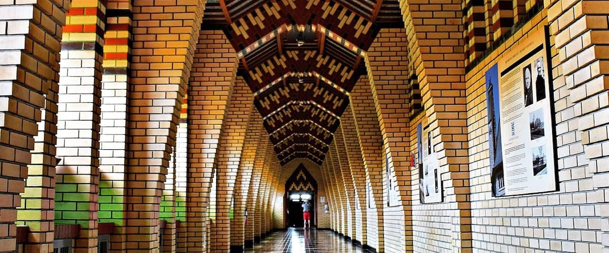 A long, arched brick corridor with patterned floor tiles and informational posters on the walls.