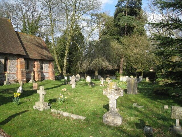 A church with a brick exterior and a grassy cemetery with numerous gravestones.