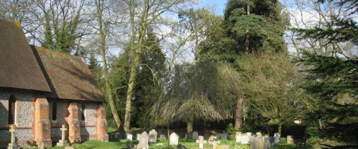 A church with a brick exterior and a grassy cemetery with numerous gravestones.