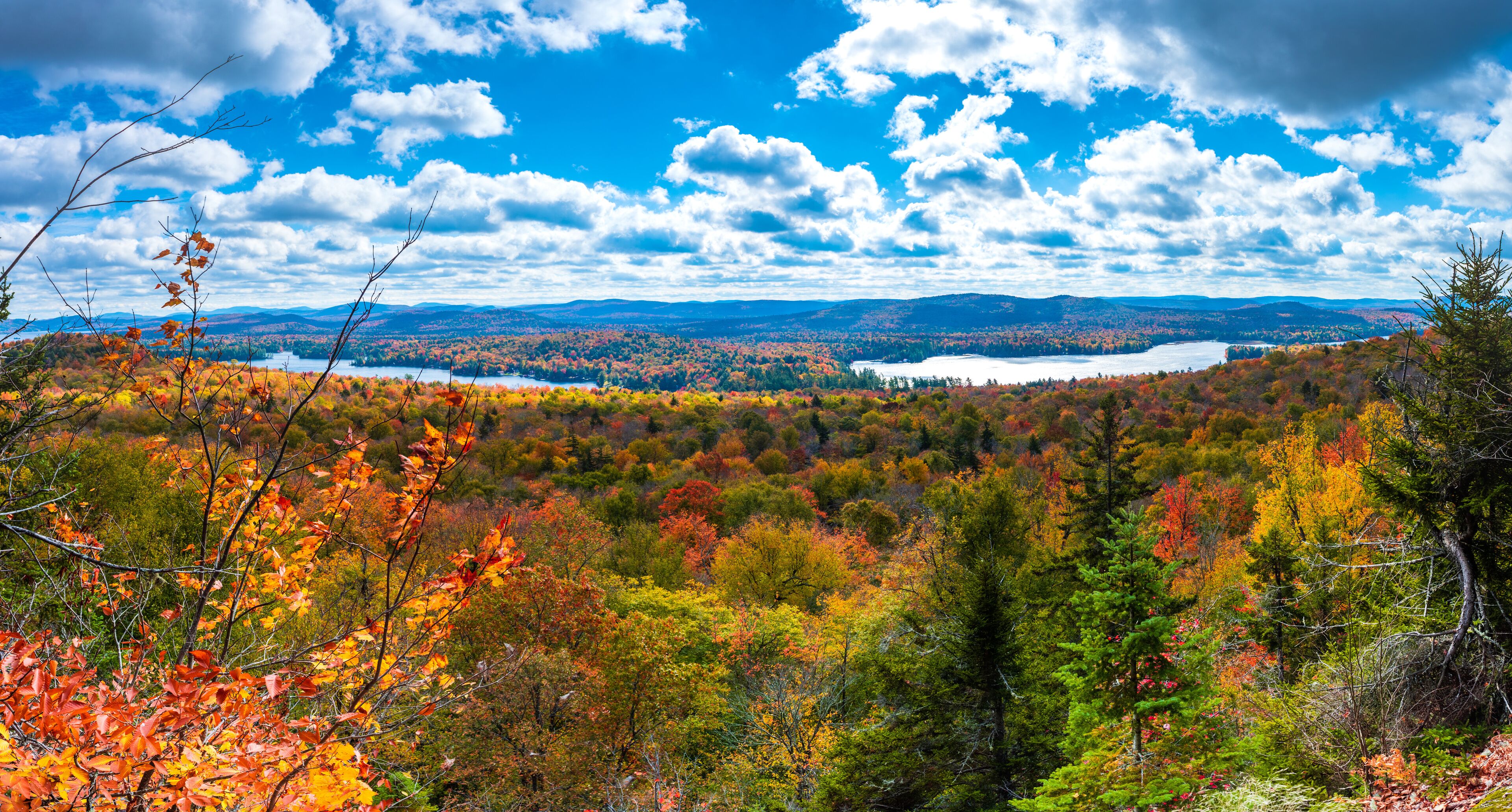 A landscape with autumn foliage, a lake, and distant mountains under a partly cloudy sky.