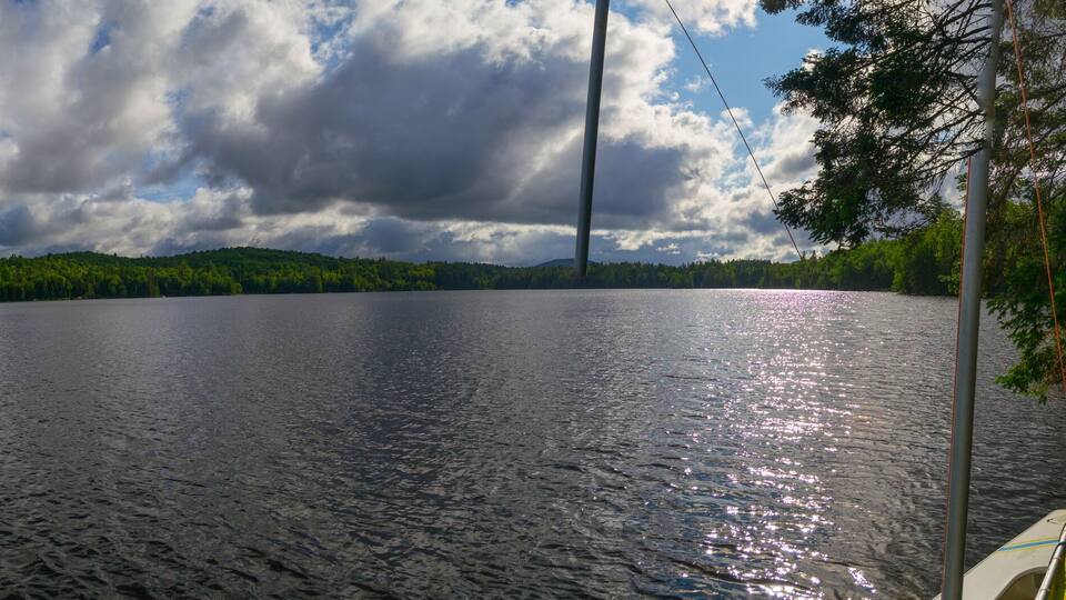 A calm lake with a forested shoreline and a cloudy sky.