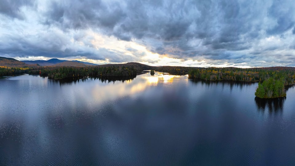 A calm lake surrounded by forested hills under a cloudy sky.