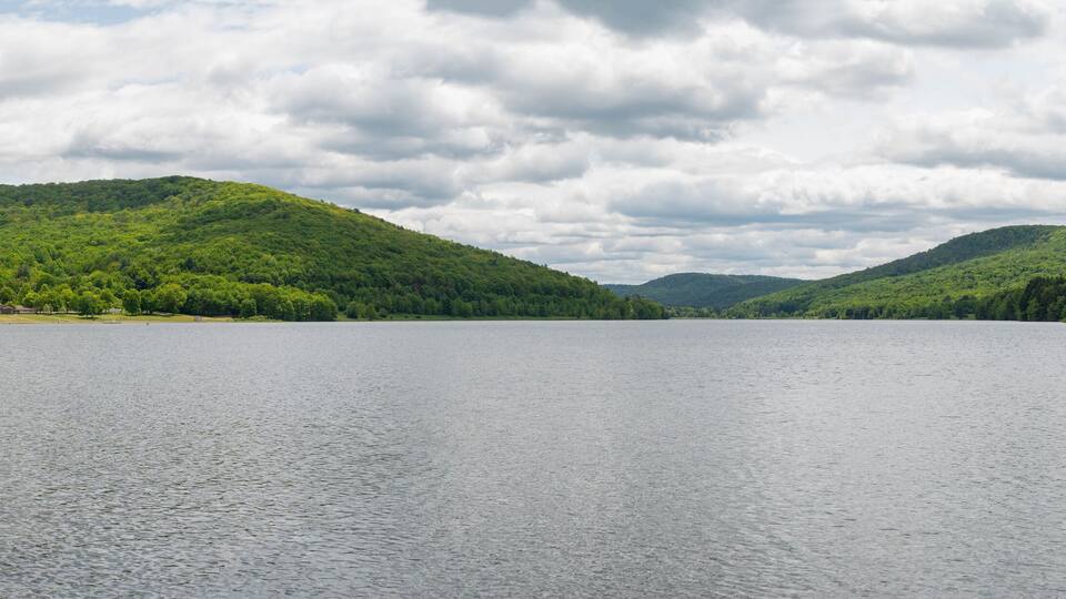 A calm lake surrounded by lush green hills under a cloudy sky.
