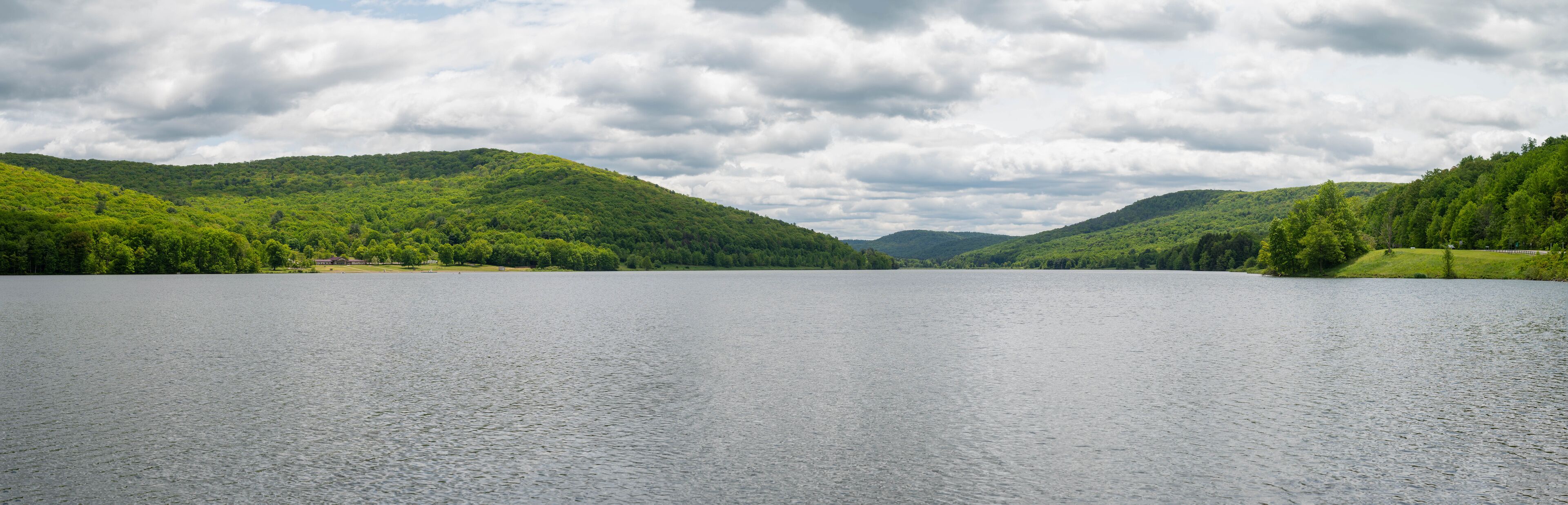 A calm lake surrounded by lush green hills under a cloudy sky.