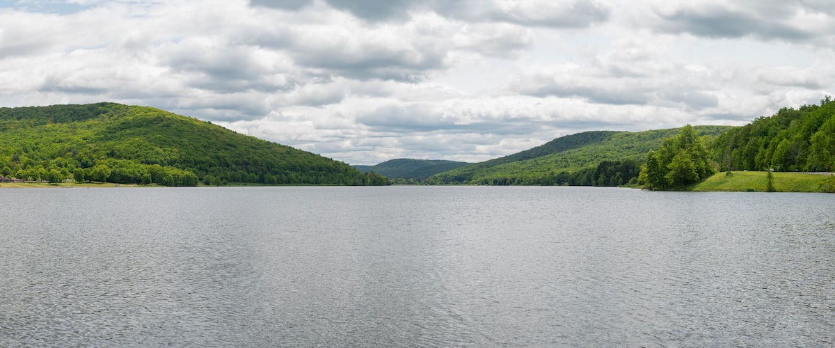 A calm lake surrounded by lush green hills under a cloudy sky.
