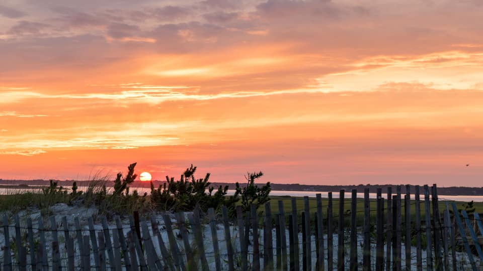 A sunset over a beach with a wooden fence in the foreground.
