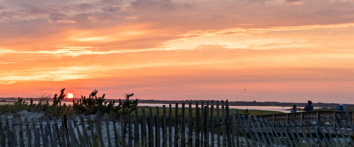 A sunset over a beach with a wooden fence in the foreground.