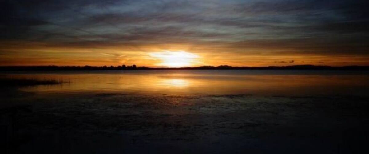 A sunset over a calm lake with a silhouette of trees in the distance.