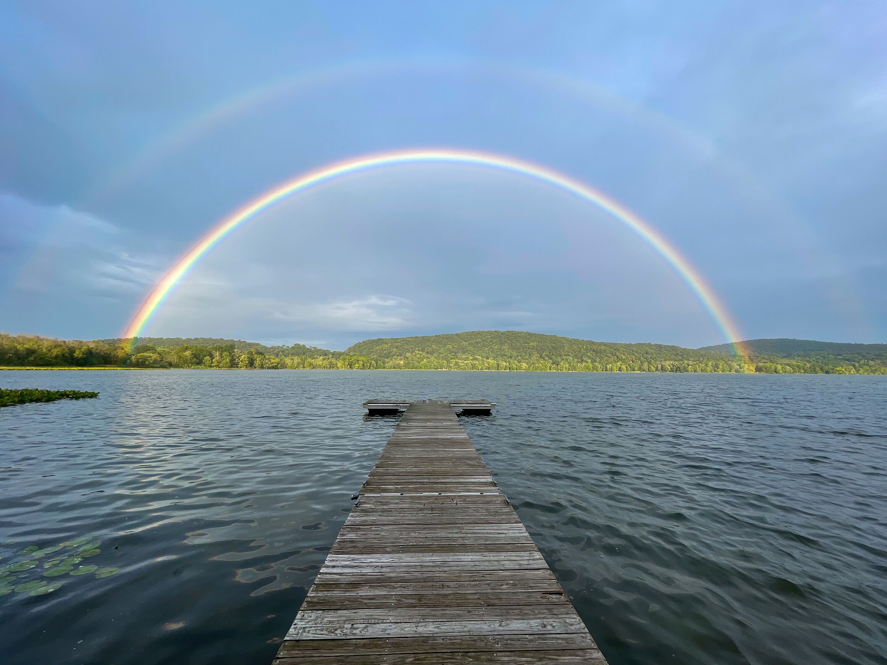 Congers, NY - USA - August 8, 2021: Landscape view of a rainbow over Rockland Lake in Rockland Lake State Park during the golden hour.