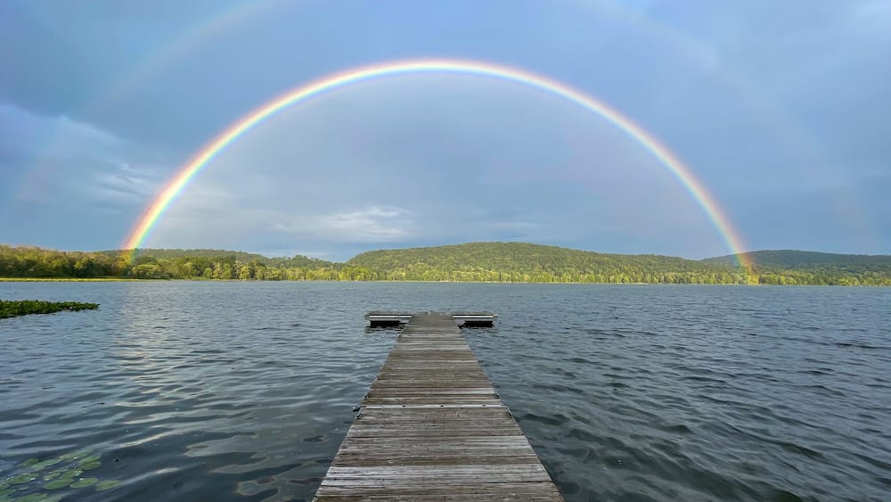 Une jetée en bois s’avançant dans un lac, avec un arc-en-ciel qui la surplombe.