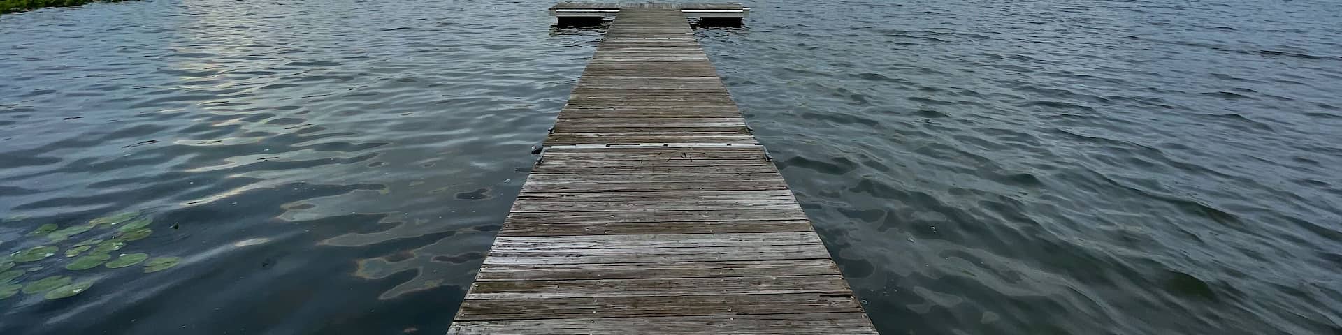 A wooden dock extending into a lake with a rainbow arching over it.