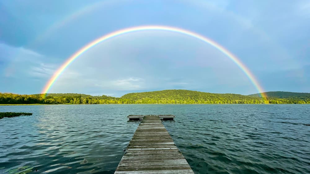 Congers, NY - USA - August 8, 2021: Landscape view of a rainbow over Rockland Lake in Rockland Lake State Park during the golden hour.