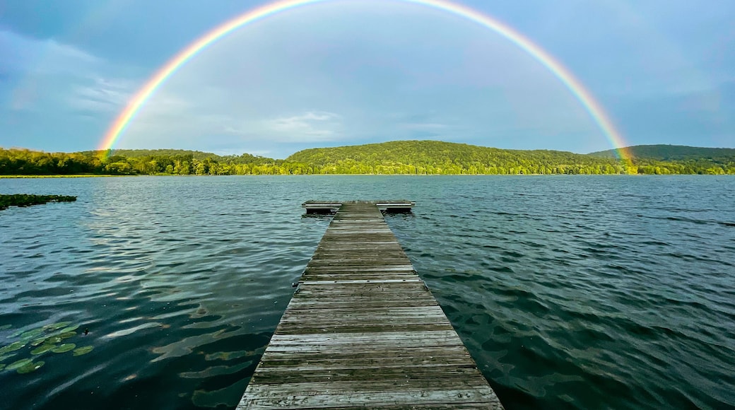 Congers, NY - USA - August 8, 2021: Landscape view of a rainbow over Rockland Lake in Rockland Lake State Park during the golden hour.
