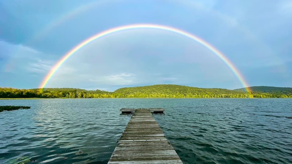 A wooden dock extending into a lake with a rainbow arching over it.