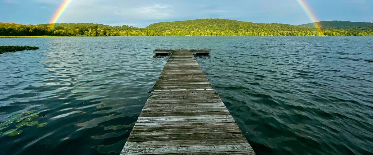 A wooden dock extending into a lake with a rainbow arching over it.