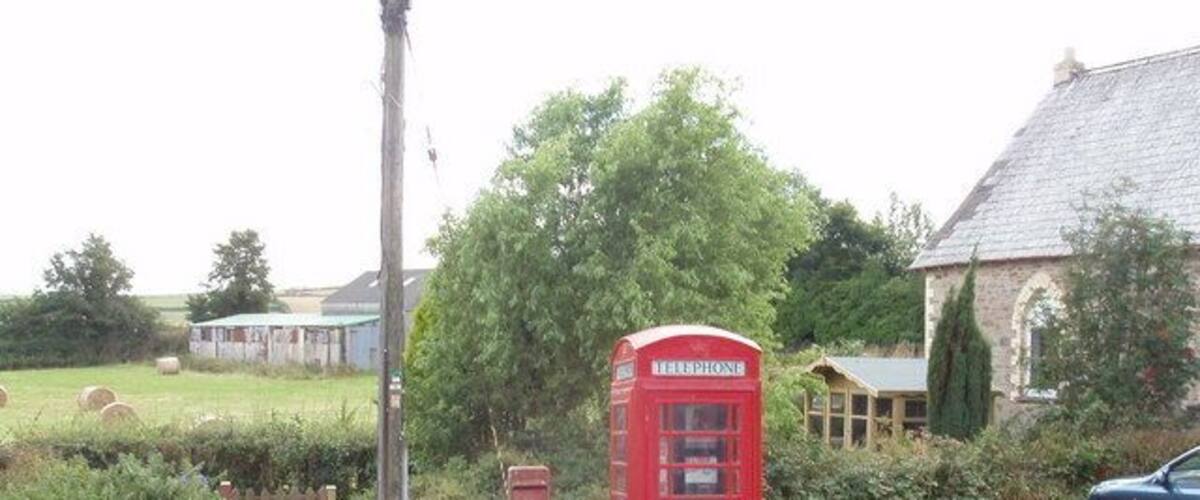 A rural landscape with a red telephone booth, a blue car, and a stone building.