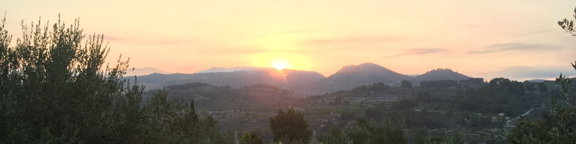 A sunset over a hilly landscape with a view of a garden and a building in the foreground.