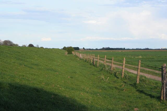 A grassy field with a wooden fence and a dirt path.