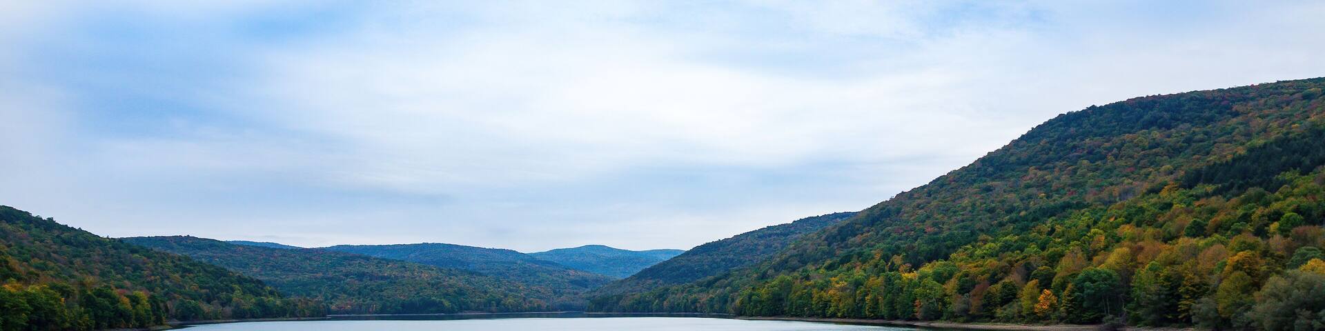 Pepacton Reservoir, Catskills, NY. Beautiful calm lake surrounded by forest. Colors of the leaves are starting to change with Autumn season, and reflections in the water. Blue sky, Wide shot.