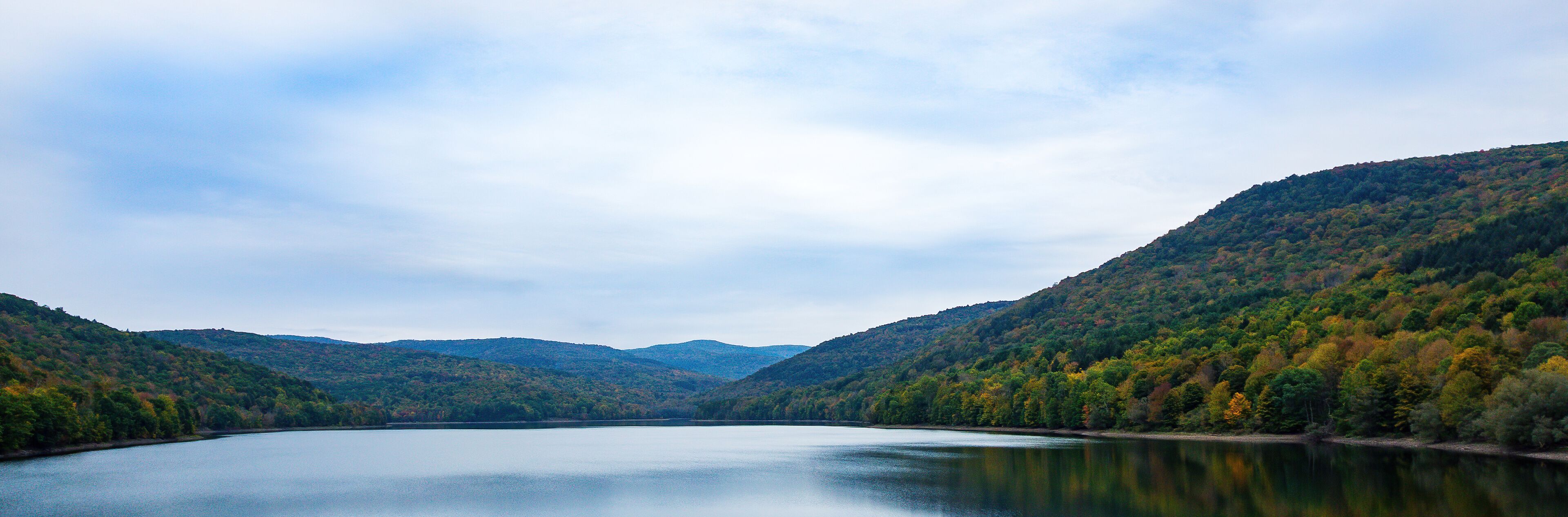 A calm lake surrounded by forested hills.