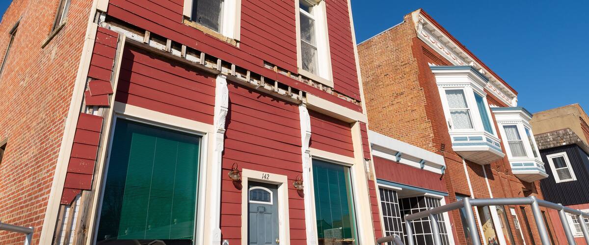 A red brick building with a blue door and green shutters, number 142, with a clear blue sky in the background.