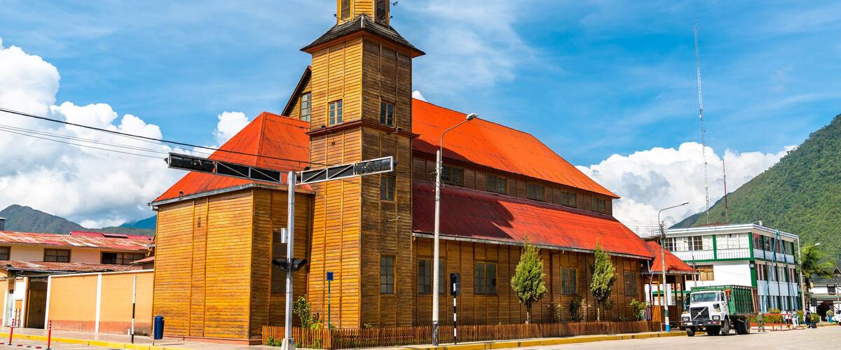 A wooden church with a red roof and a cross on top, surrounded by mountains.