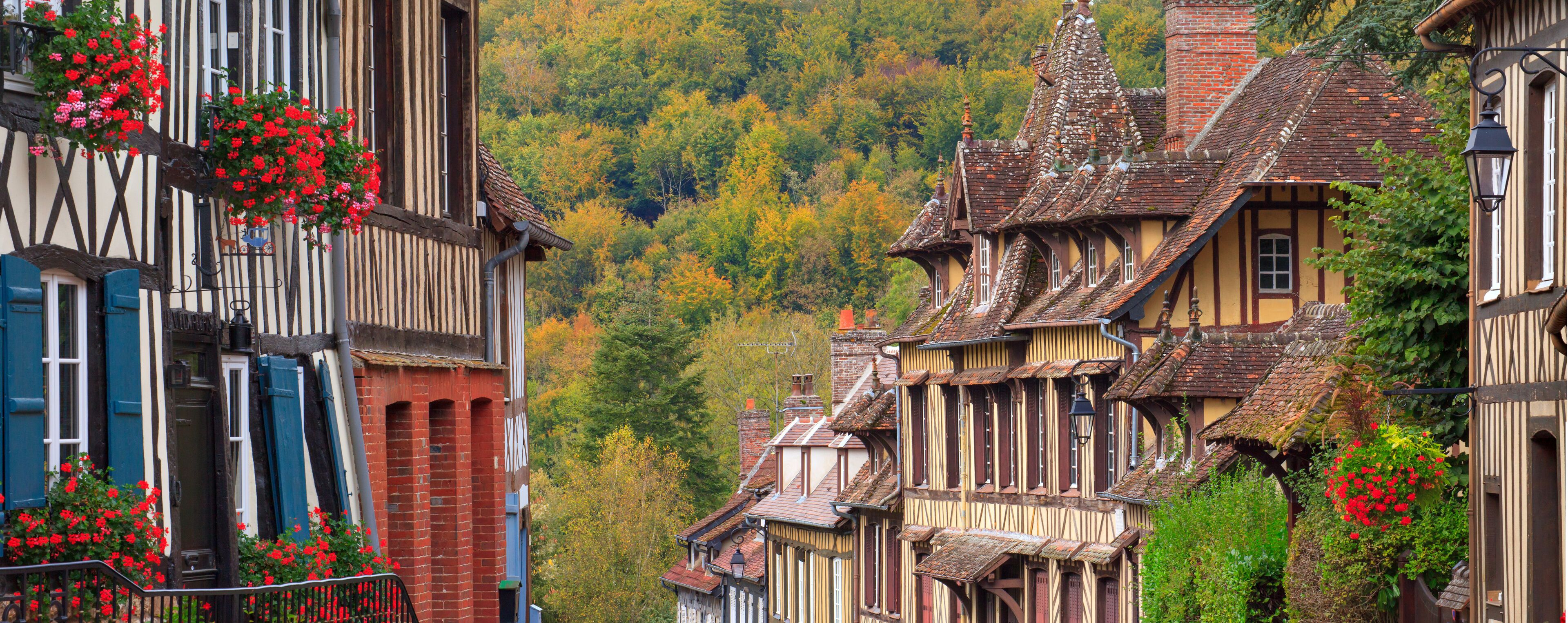 A narrow street lined with traditional half-timbered houses, steeply pitched roofs, and hanging flower baskets.