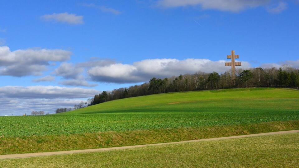 A green field with a cross-shaped structure in the distance.