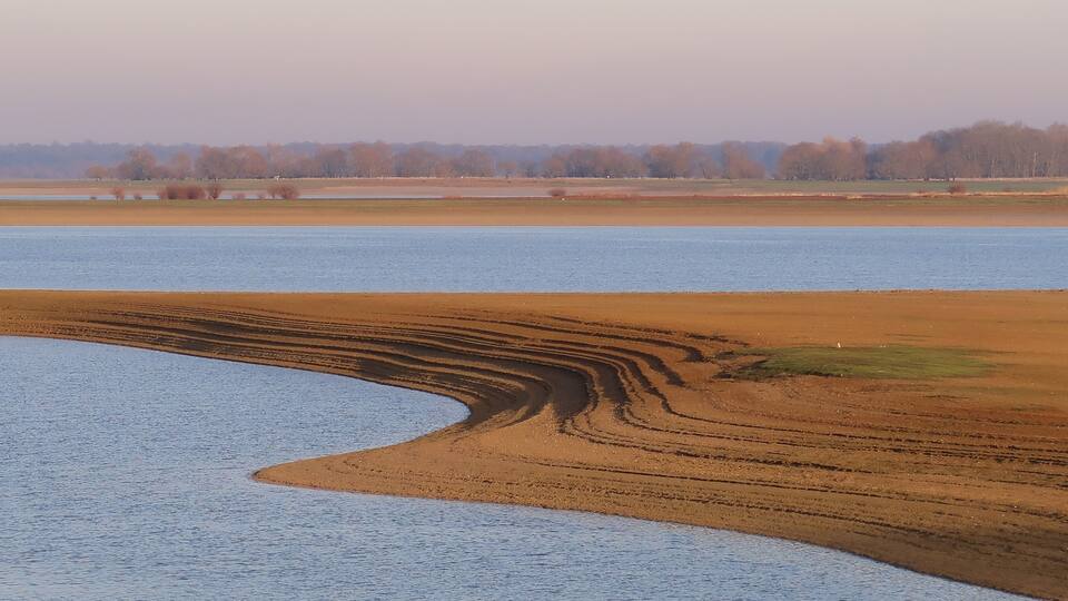 A river curving through a field with a distinct pattern of tire tracks.