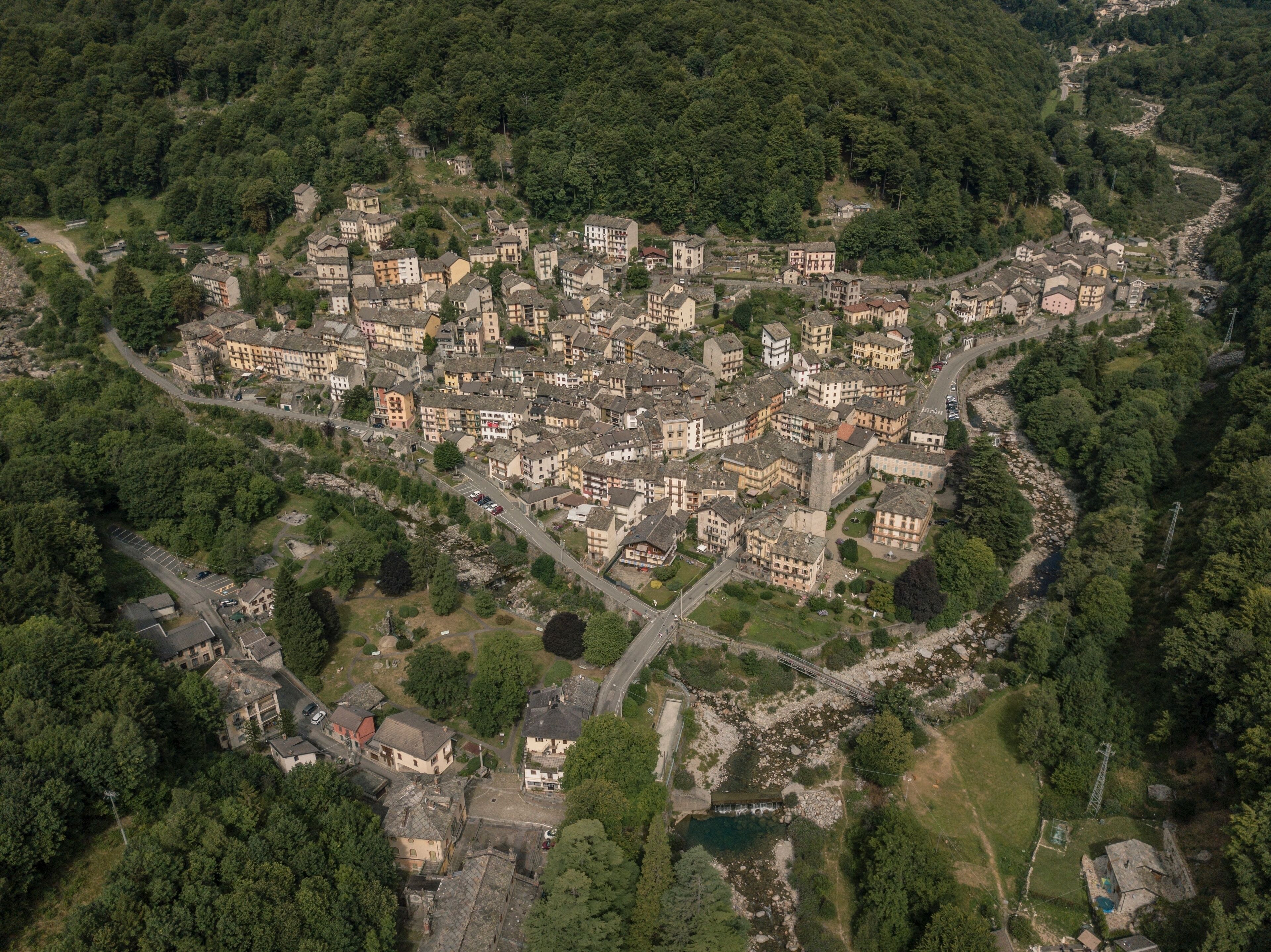 An aerial view of a historic town with dense forested hills, a winding river, and a mix of traditional and modern architecture.