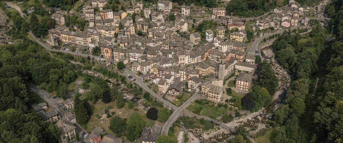 An aerial view of a historic town with dense forested hills, a winding river, and a mix of traditional and modern architecture.