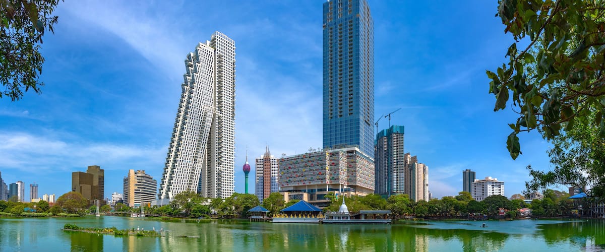 A cityscape with modern skyscrapers, a body of water, and surrounding greenery.