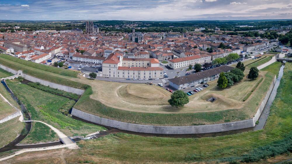 An aerial view of a historic town with a prominent castle, a cathedral, and surrounding greenery.