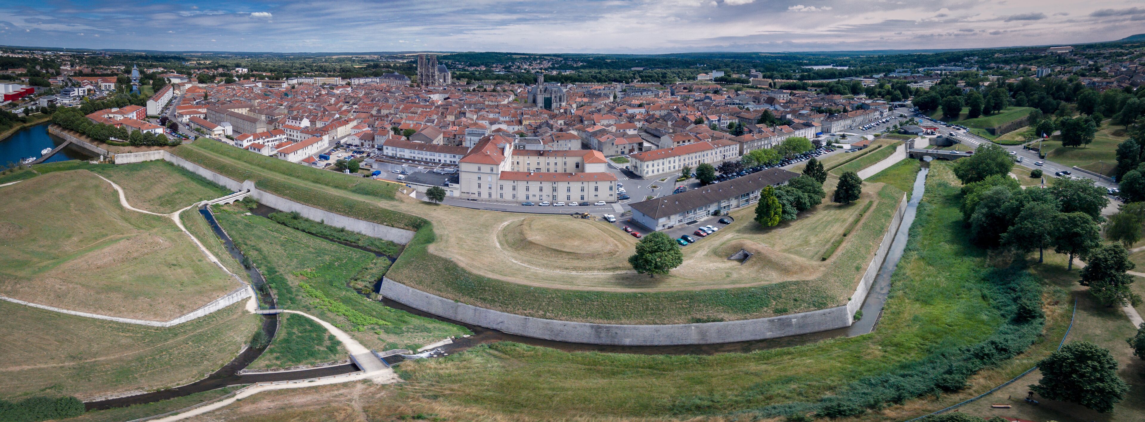 An aerial view of a historic town with a prominent castle, a cathedral, and surrounding greenery.