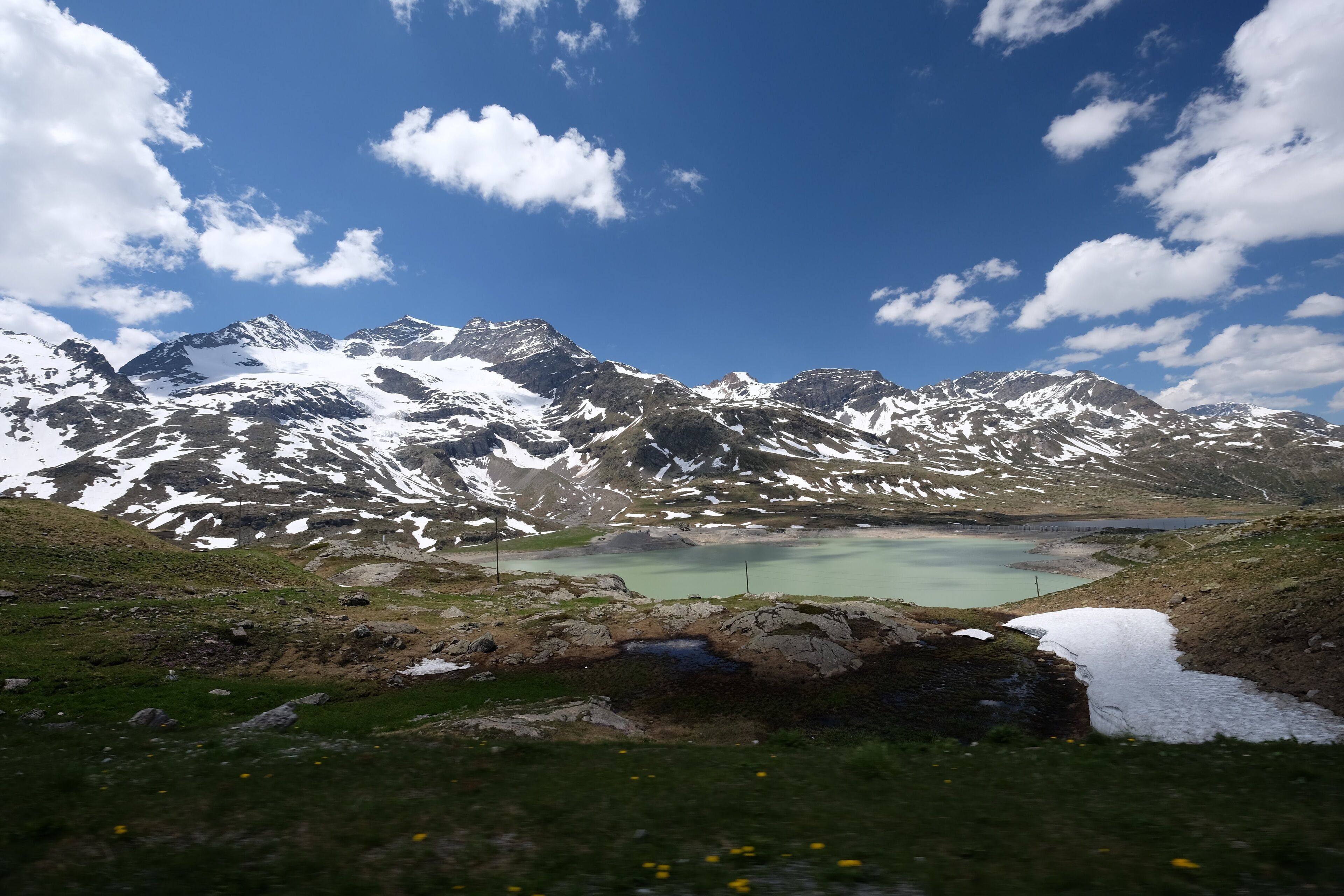 Snow-capped mountains, a turquoise lake, and a grassy foreground.
