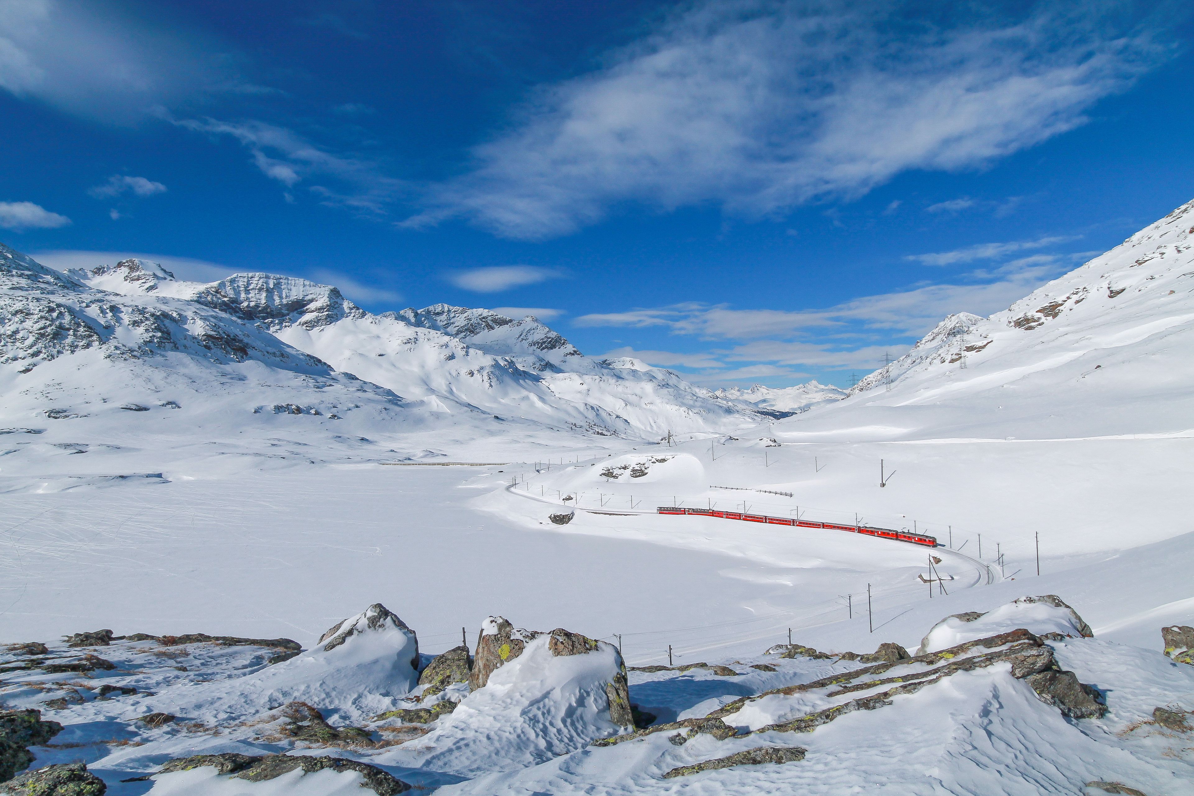 Eine verschneite Berglandschaft mit einem roten Zug in der Ferne.