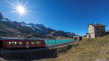 A red train on tracks, a turquoise lake, and snow-capped mountains in the background.