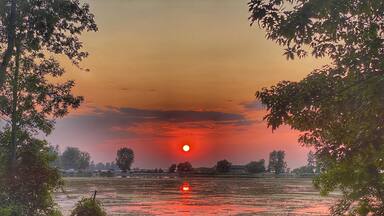 Ein Sonnenuntergang über einem See mit Bäumen am Ufer.