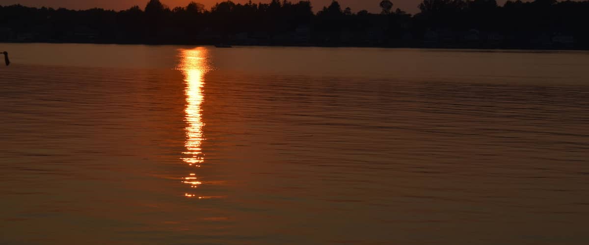 A sunset over a calm body of water with a silhouette of trees in the background.