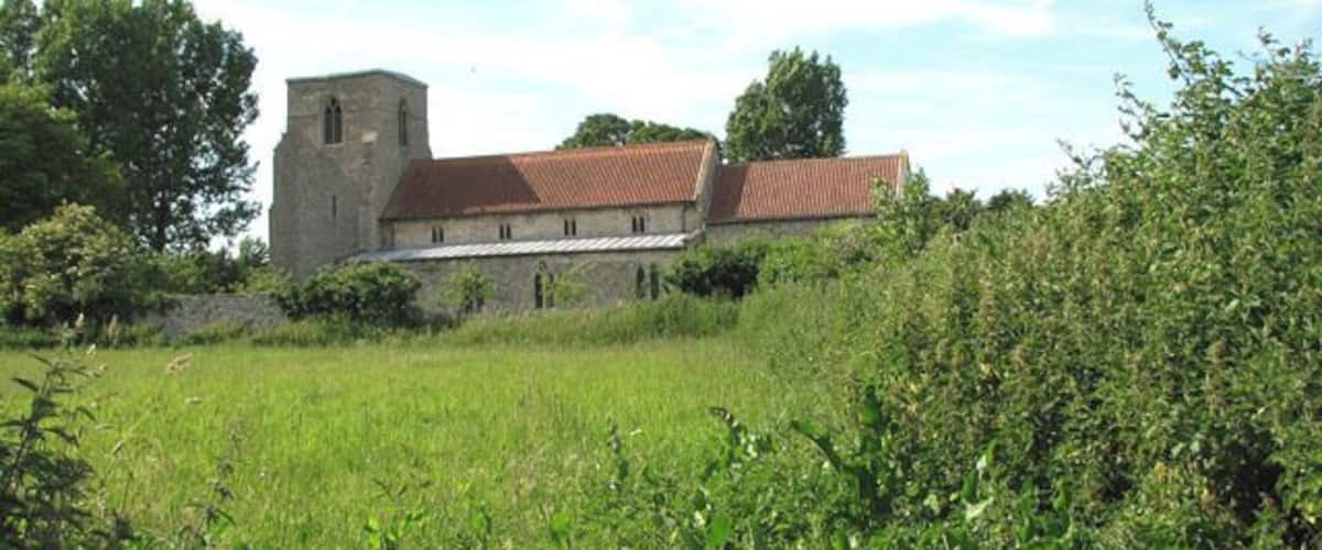 A stone building with a red roof, surrounded by lush green fields and trees.