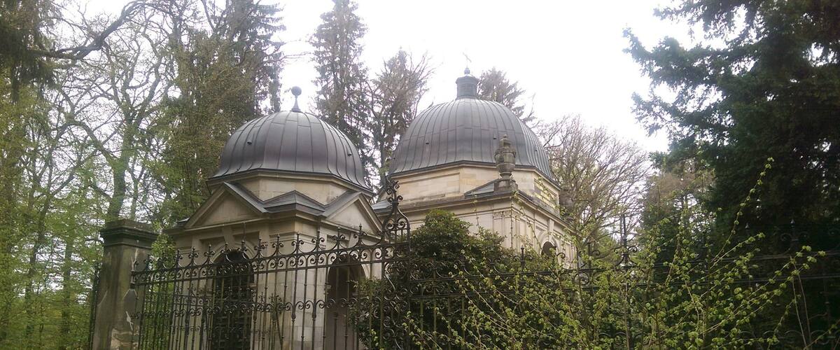 A historical building with two domed structures surrounded by a wrought iron fence and trees.