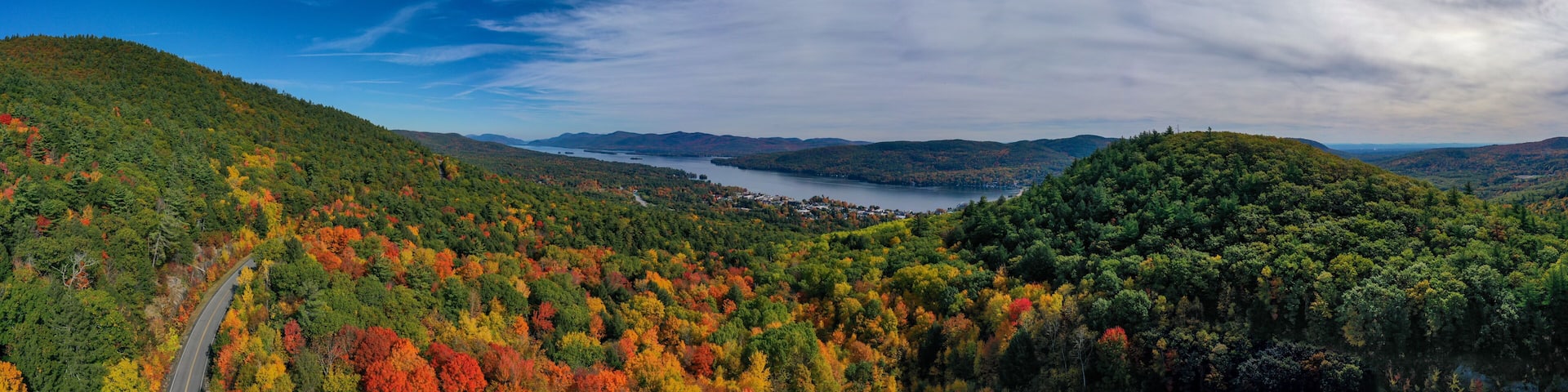 A mountainous landscape with a lake, autumn foliage, and a winding road.