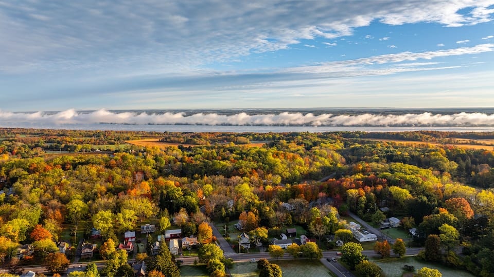 A panoramic view of a rural landscape with autumn foliage, a river, and a misty horizon.