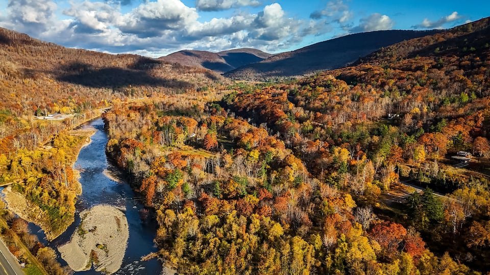 A river winding through a forested valley with autumn foliage, surrounded by hills.