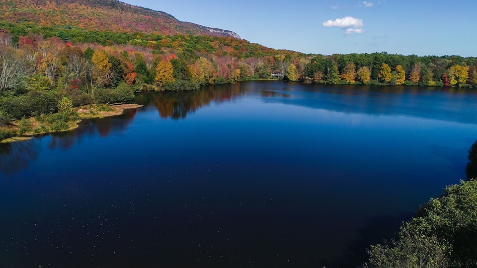 A calm lake surrounded by autumn-colored trees and a mountain in the background.